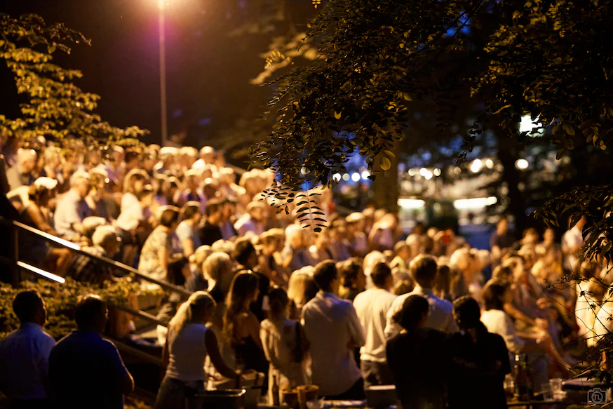 Ein Bild vom Publikum verschommen im hintergund, blätter hängen vorne ins Bild